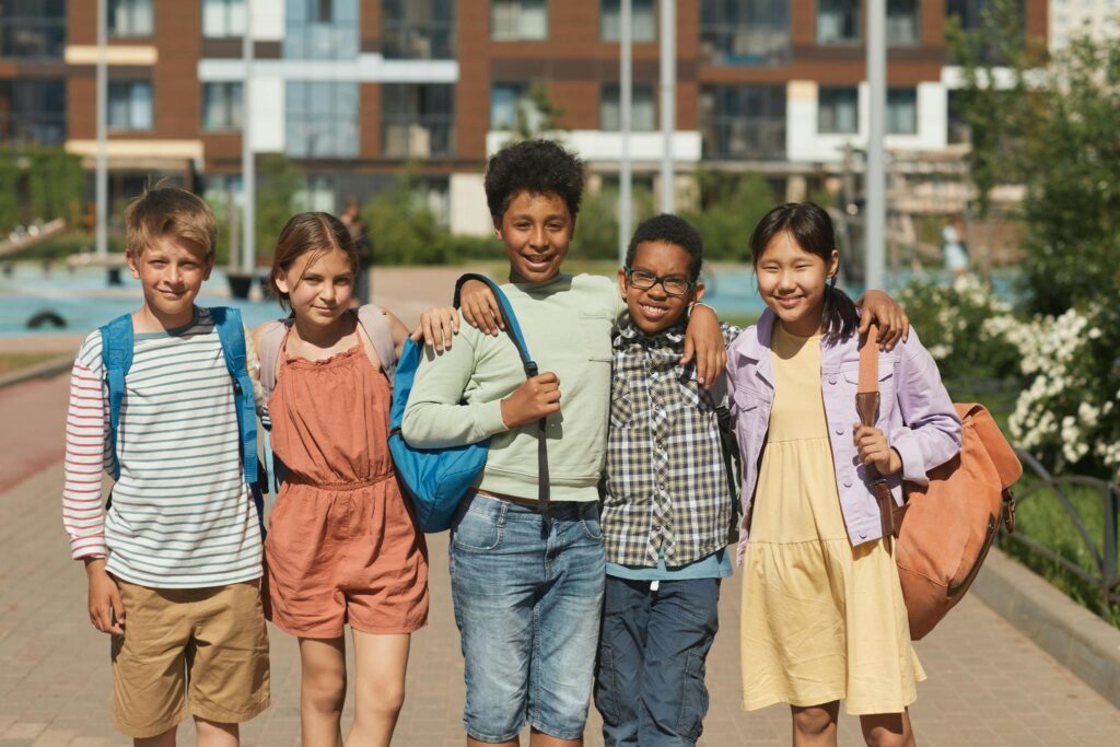 Smiling children with backpacks enjoying a sunny day in an urban setting.